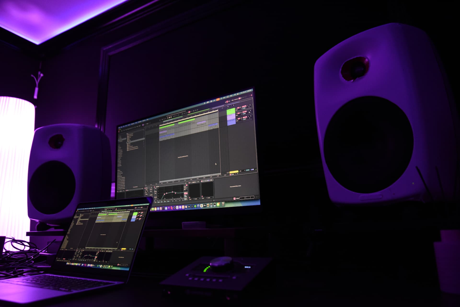 Studio desk with two white monitors, a laptop and an interface under purple neon light
