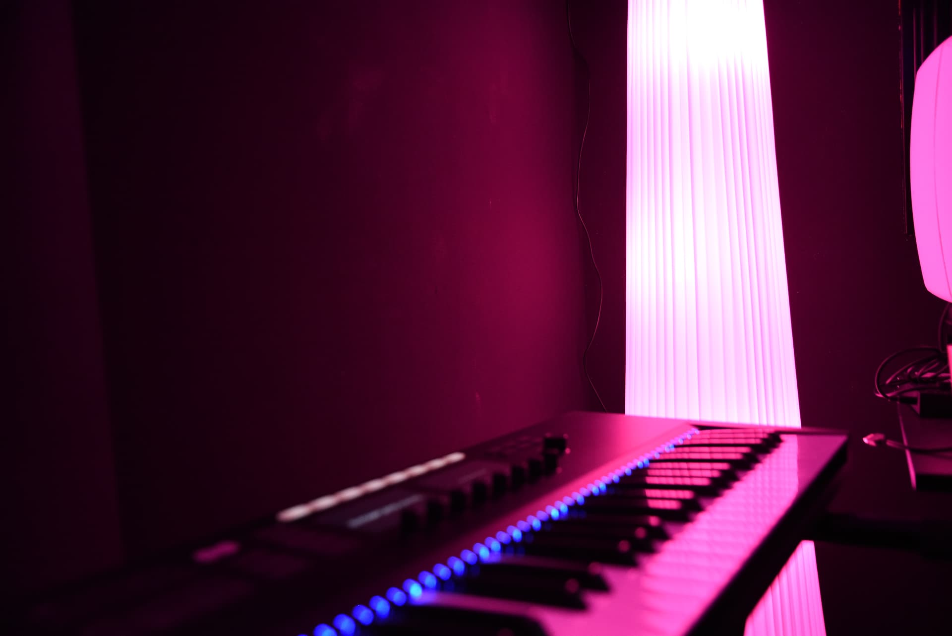 Black electric guitar leaning against a white studio monitor on a keyboard lit by magenta light