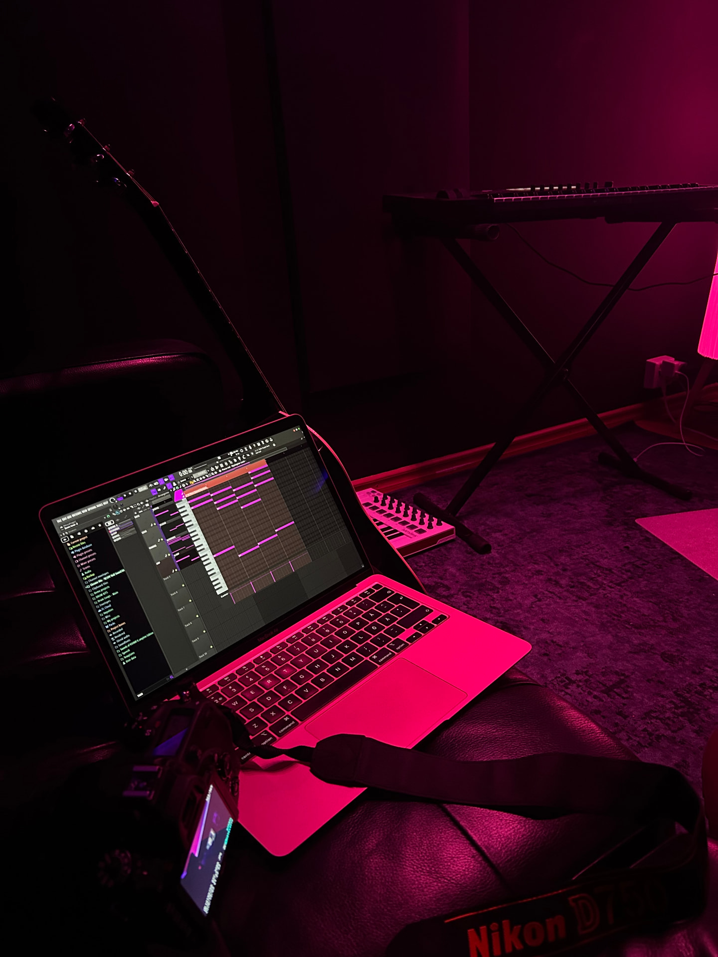 Laptop with a production session open in deep pink light beside a guitar