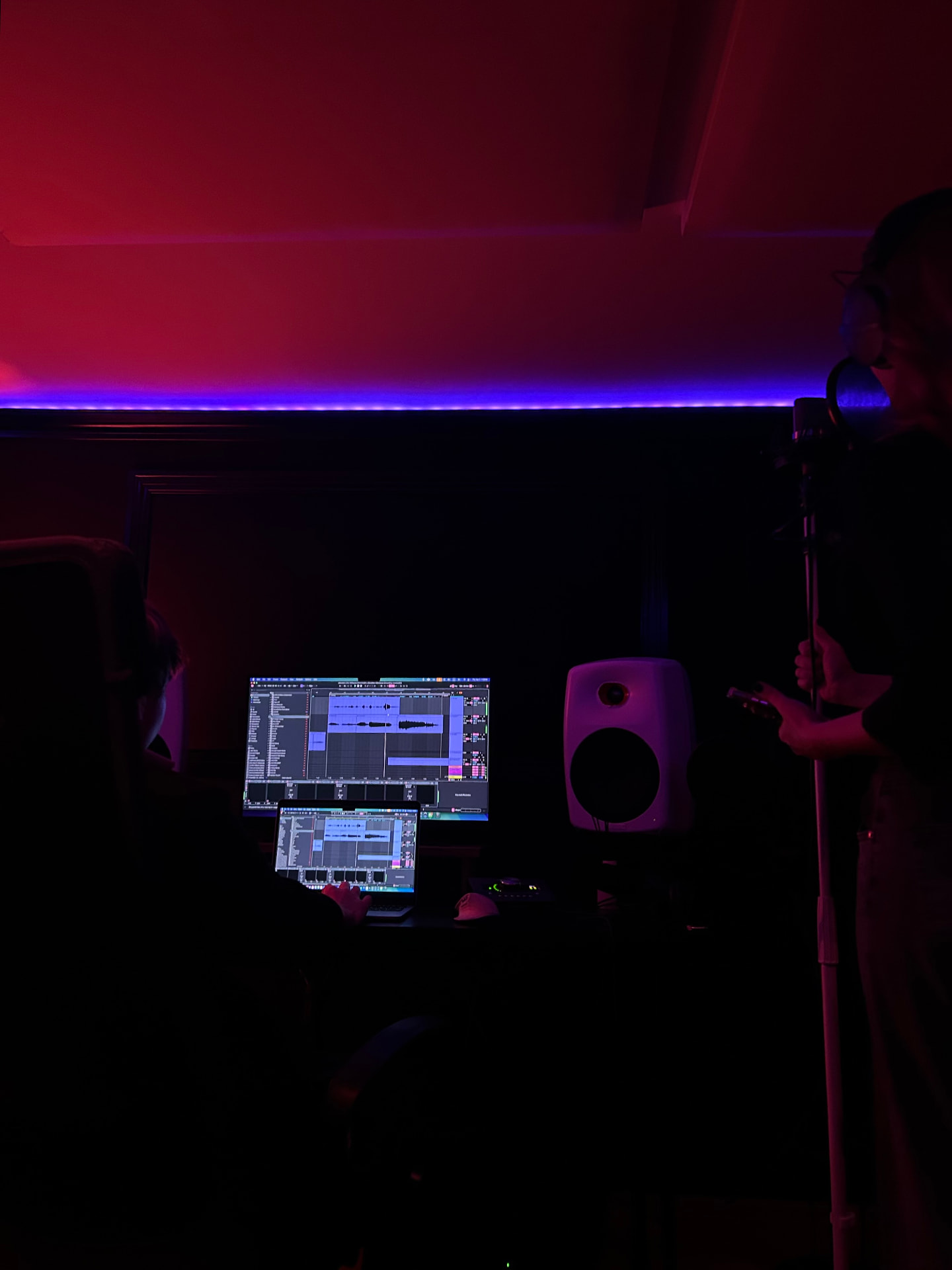 Recording a vocal take beside the mixing desk in red and blue studio light