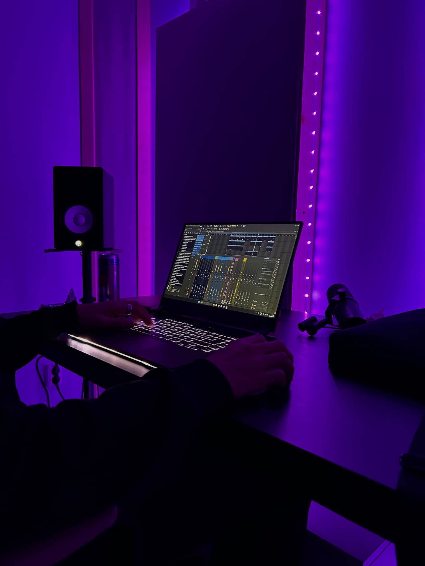 Producing a session on a laptop next to a studio monitor under purple lights