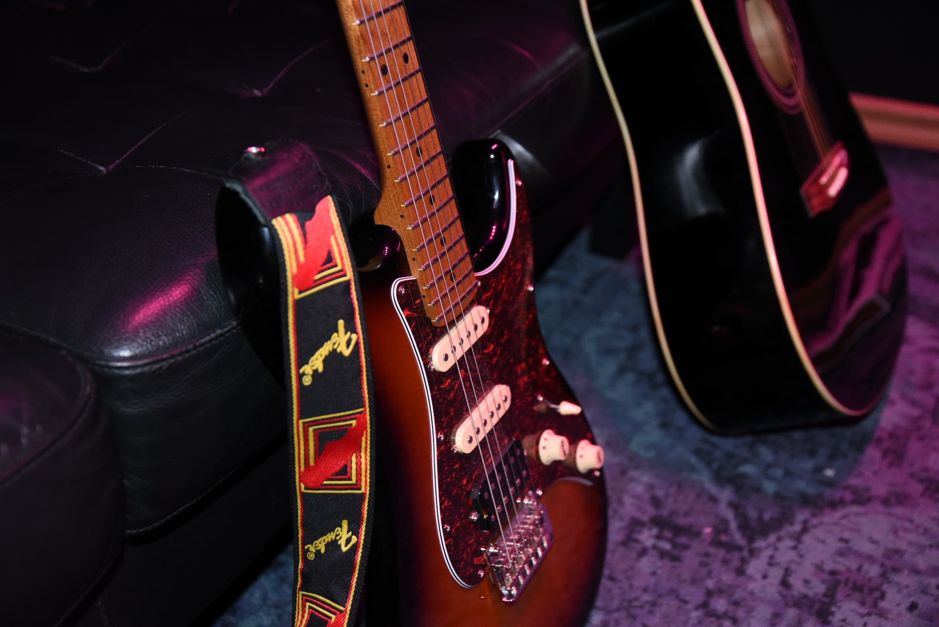 Sunburst electric guitar leaning against a black leather couch in purple and pink studio light